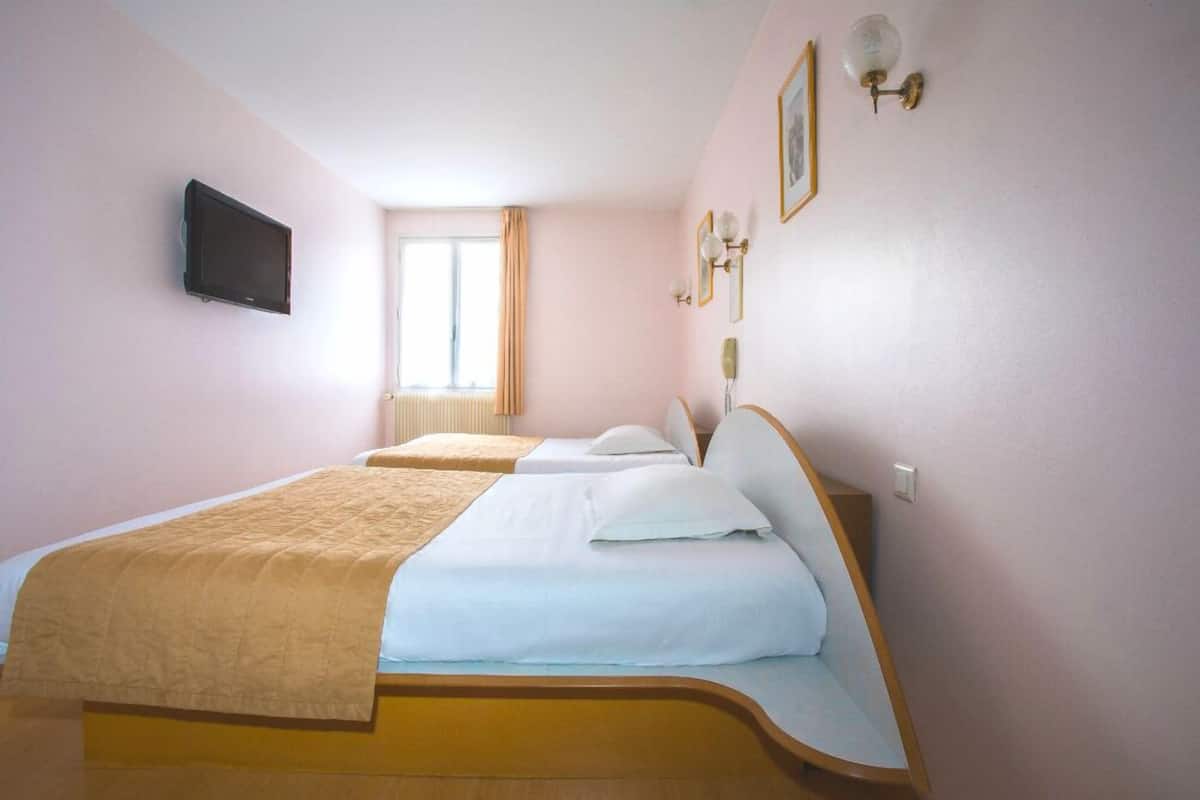 A hotel room with a bed, a TV, and a window with curtains.