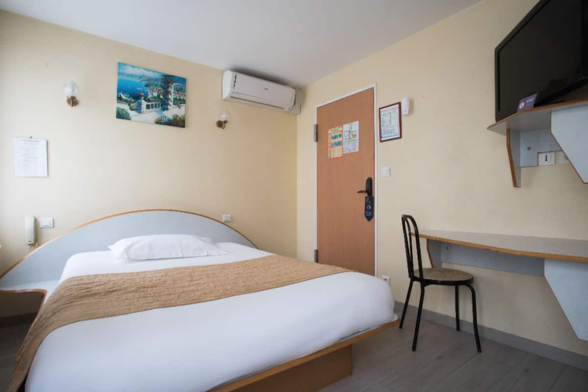 A hotel room with a bed, a desk, a chair, an air conditioner, and a television.