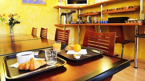 A breakfast tray with croissant, orange juice, and coffee on a table in a room with yellow walls, wooden chairs, and a TV on a shelf. - Hôtel de Rosny (Tours)