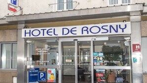 A hotel entrance with a sign reading "HOTEL DE ROSNY". There are flags, a parking sign, and a glass door entrance. - Hôtel de Rosny (Tours)