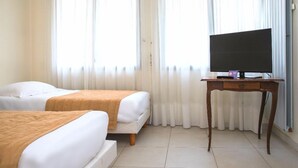 A hotel room with two beds, a TV on a wooden table, and large windows with sheer curtains. - Hôtel de Rosny (Tours)