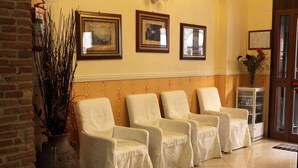 A reception area with four white armchairs, a vase with dried plants, and framed pictures on the wall. - Hollywood Roma (Rome)