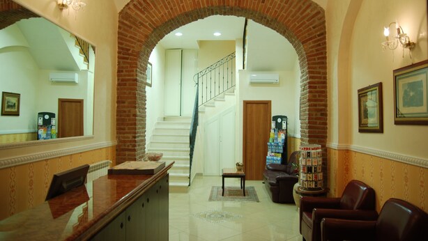 A reception area with a brick archway, a staircase, a reception desk, and a seating area with a coffee machine. - Hollywood Roma (Rome)