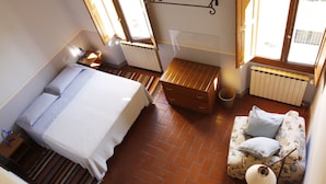 A bedroom with a bed, a small wooden chest, a sofa with cushions, a radiator, and a window with a view of the outside. - Gianna's B&B (Florence)