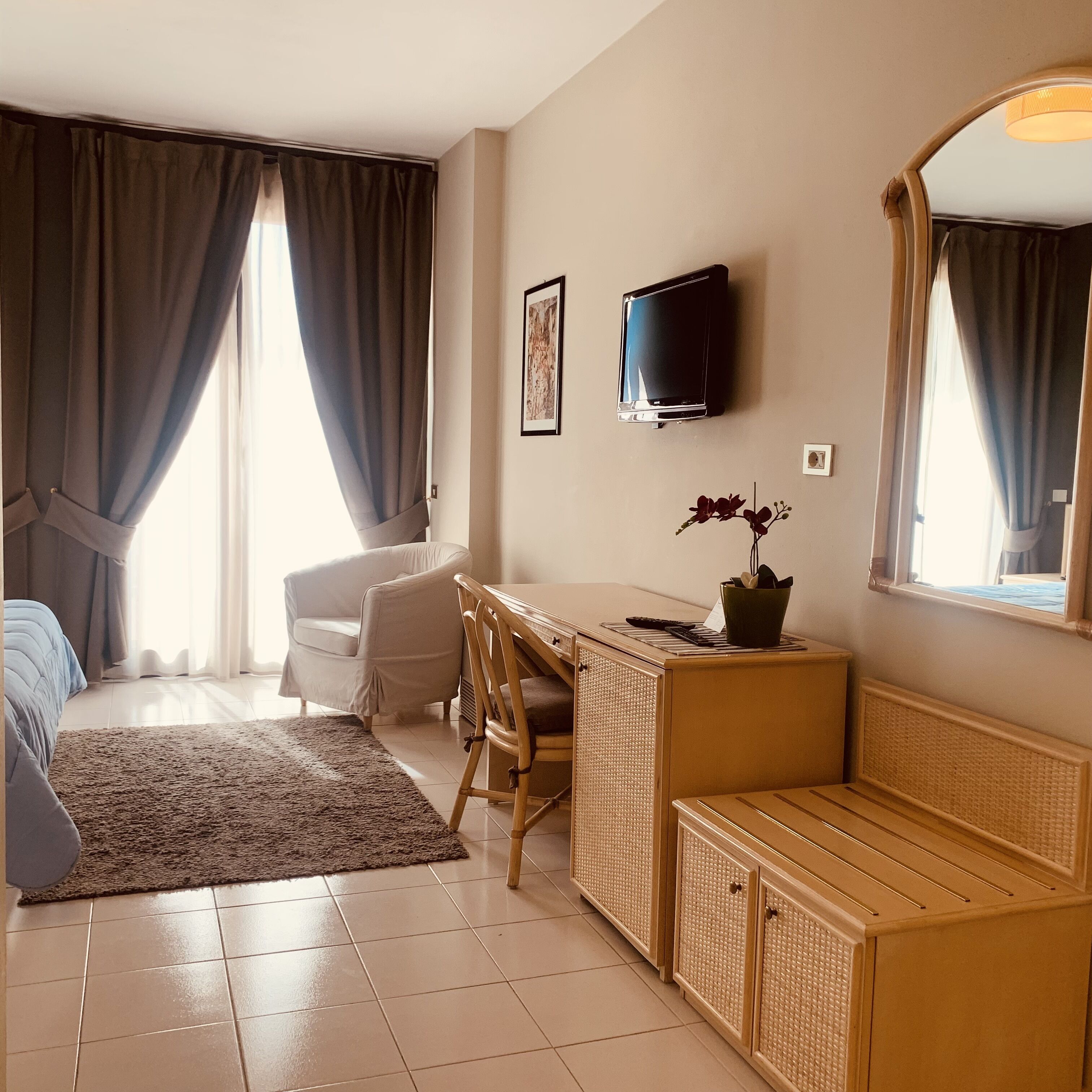 Habitación de hotel con cama, escritorio, silla, televisor y un ventanal con cortinas.