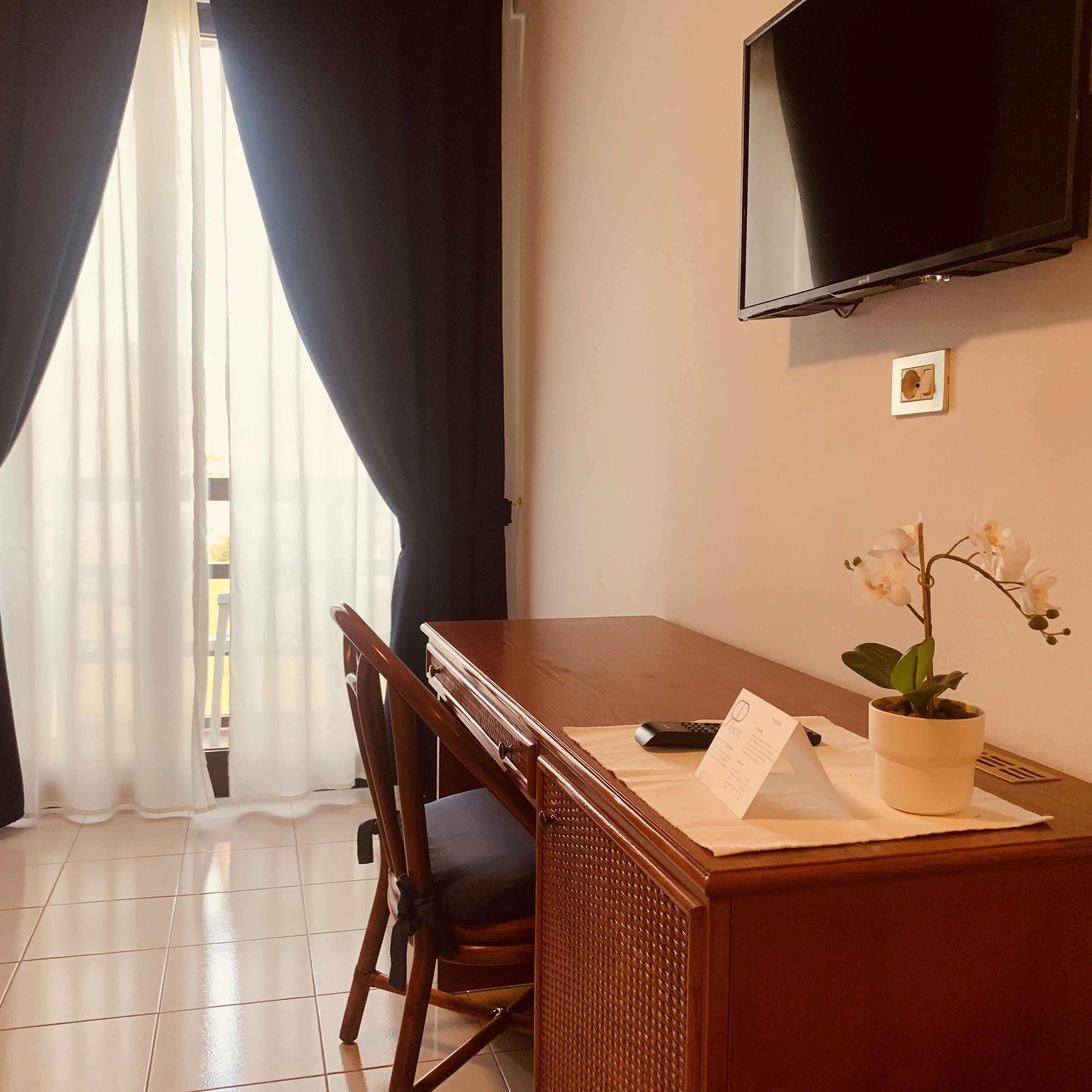 Habitació d'hotel amb taula de dinar de fusta, cadires, una orquídia en test i comandament a distància, i televisió de pantalla plana penjada a la paret.