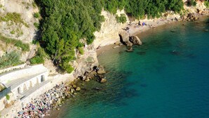 Vue aérienne d’une zone côtière avec une plage, une côte rocheuse et un bâtiment blanc doté d’arcades.