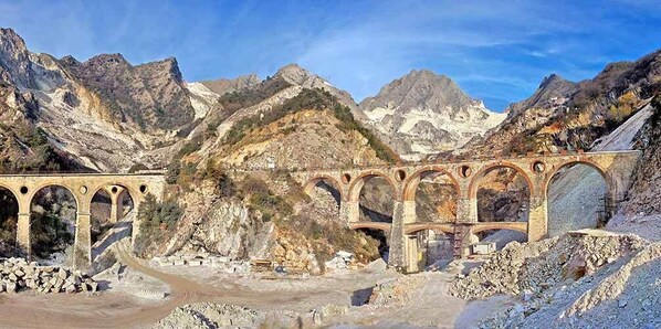 Un puente de piedra con múltiples arcos que cruza un valle, rodeado de montañas escarpadas.