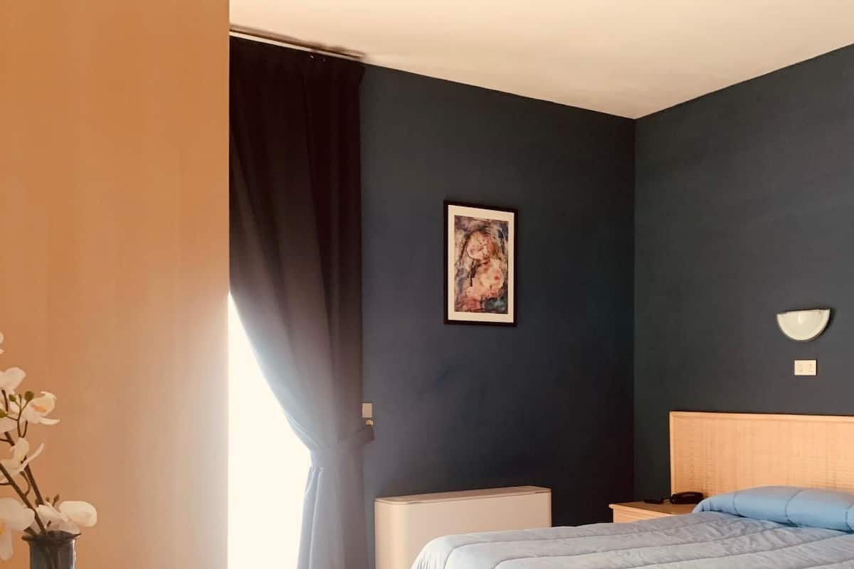 A bedroom with a bed, a nightstand, a lamp, a vase with flowers, and a painting on the wall.