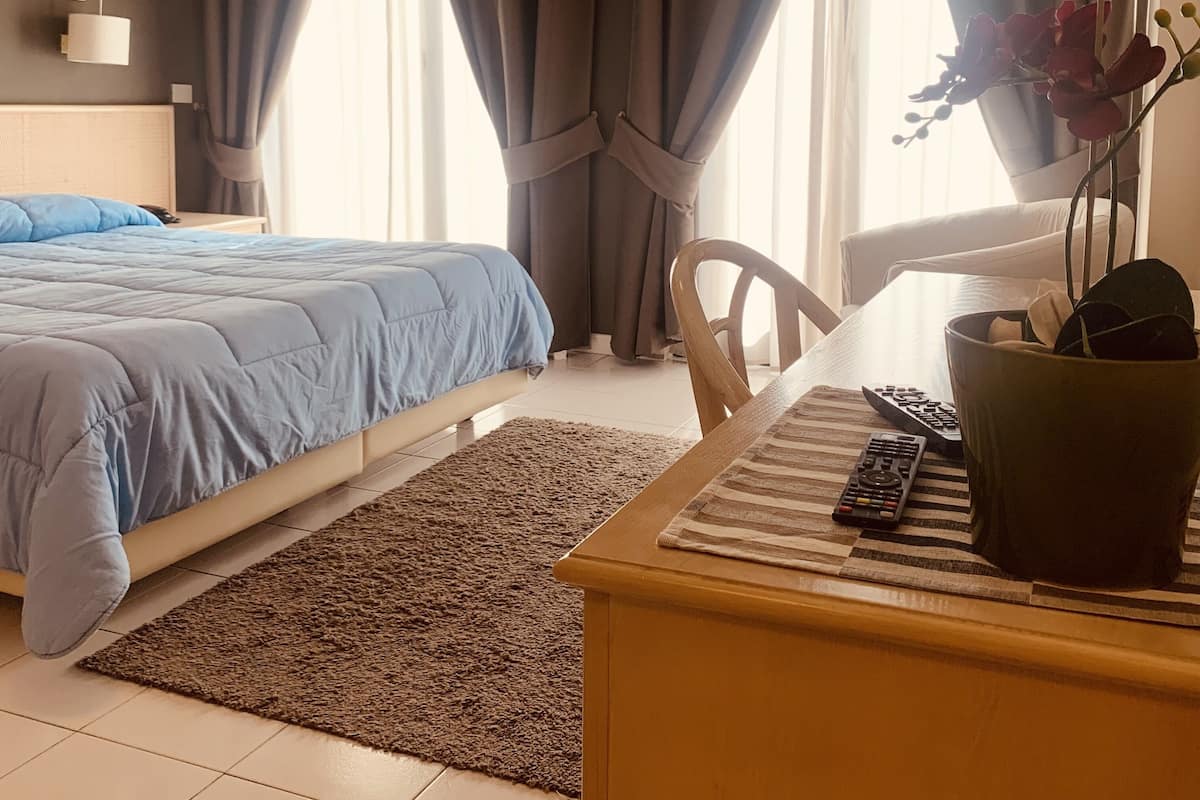 A bedroom with a bed, a desk with a keyboard, a chair, and a potted plant.