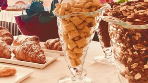Une table mise pour le petit-déjeuner avec des viennoiseries, des céréales et des fleurs.