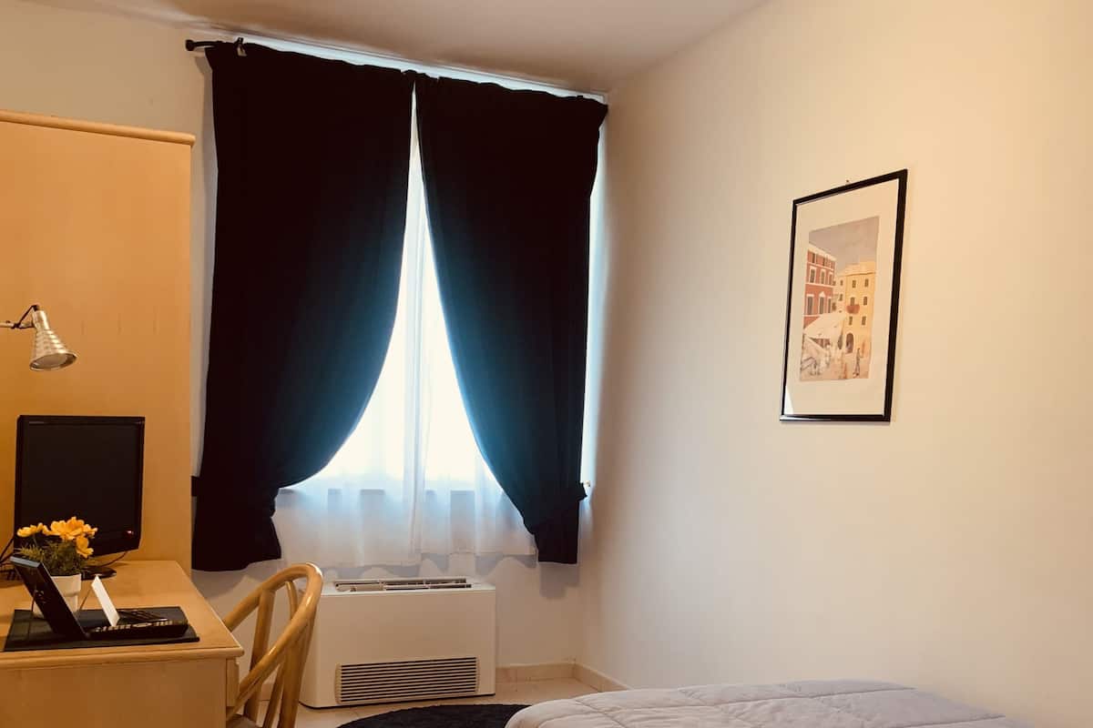 A room with a bed, a desk, a chair, a radiator, a lamp, and a framed picture on the wall.