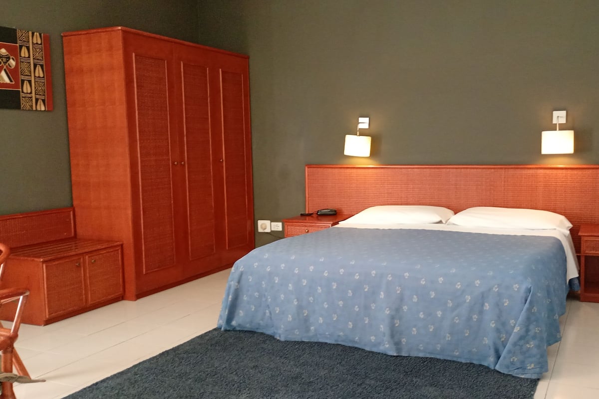 A bedroom with a bed, nightstands, a desk, a wardrobe, and a wall-mounted lamp.