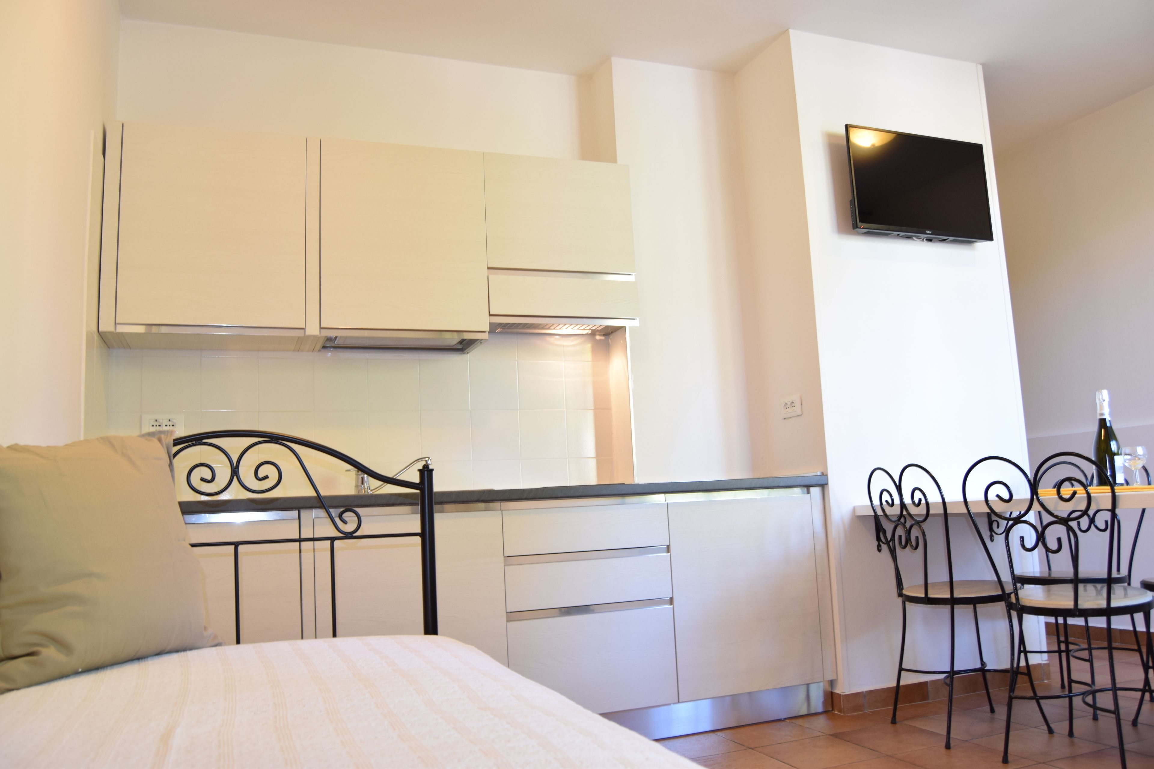 A compact bedroom with a bed, a small kitchenette, and a dining area with two chairs.