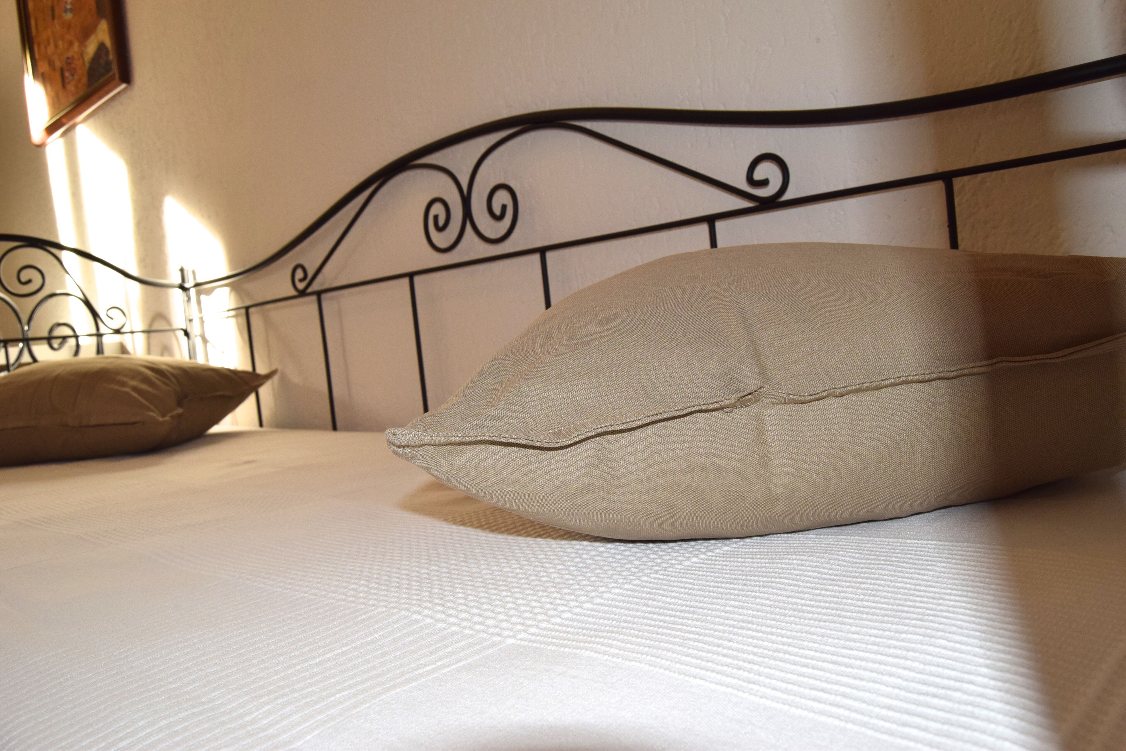 Een opgemaakt bed met hoofdbord, kussens en een gewatteerde sprei.