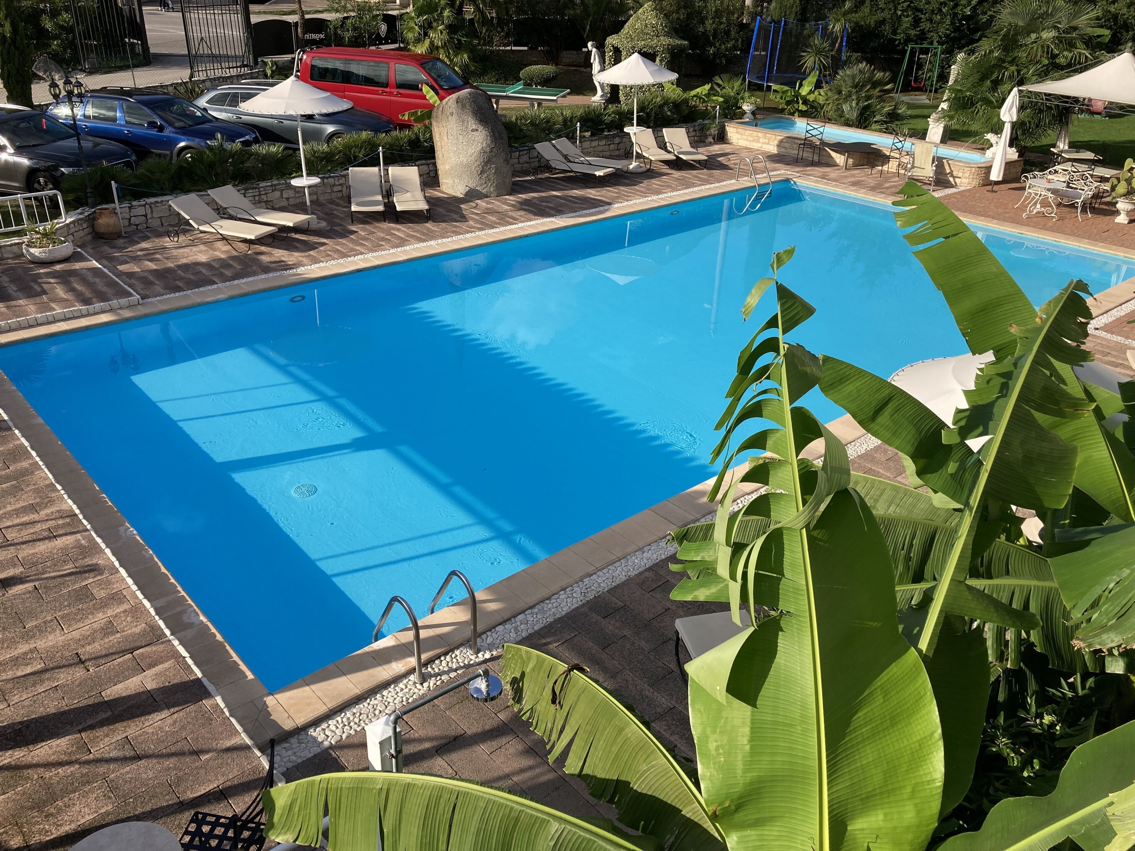 A rectangular swimming pool with clear blue water, surrounded by lounge chairs and umbrellas, with a stone pathway leading to the pool.
