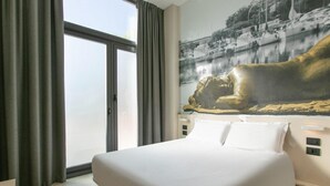 Habitación de hotel con una cama grande, vista al mar a través de una ventana y un cuadro de una figura reclinada en la pared.