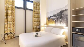 Una habitación de hotel con una cama grande, un escritorio y un televisor montado en la pared.
