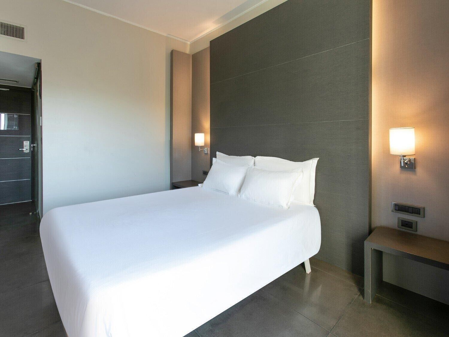 Una habitación de hotel moderna con una cama grande, una mesita de noche y dos lámparas de pared.