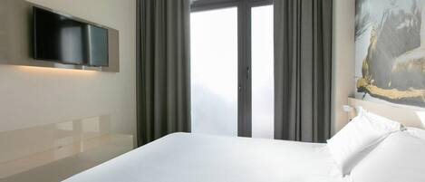 Habitación de hotel con una cama grande, un televisor de pantalla plana en la pared y una ventana con cortinas.