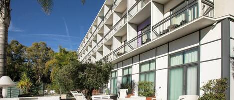 Un hotel moderno con varios balcones, mobiliario exterior y abundante vegetación.