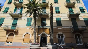 A building with multiple balconies, large potted plants, and a bicycle parked outside. - Hotel Nazionale (Levanto)