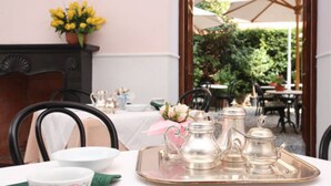 A dining table set with a tray, silverware, and a teapot, with a vase of yellow flowers on the wall. - Hotel Nazionale (Levanto)