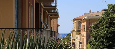 A row of multi-story buildings with balconies, a palm tree in the foreground, and a clear blue sky.