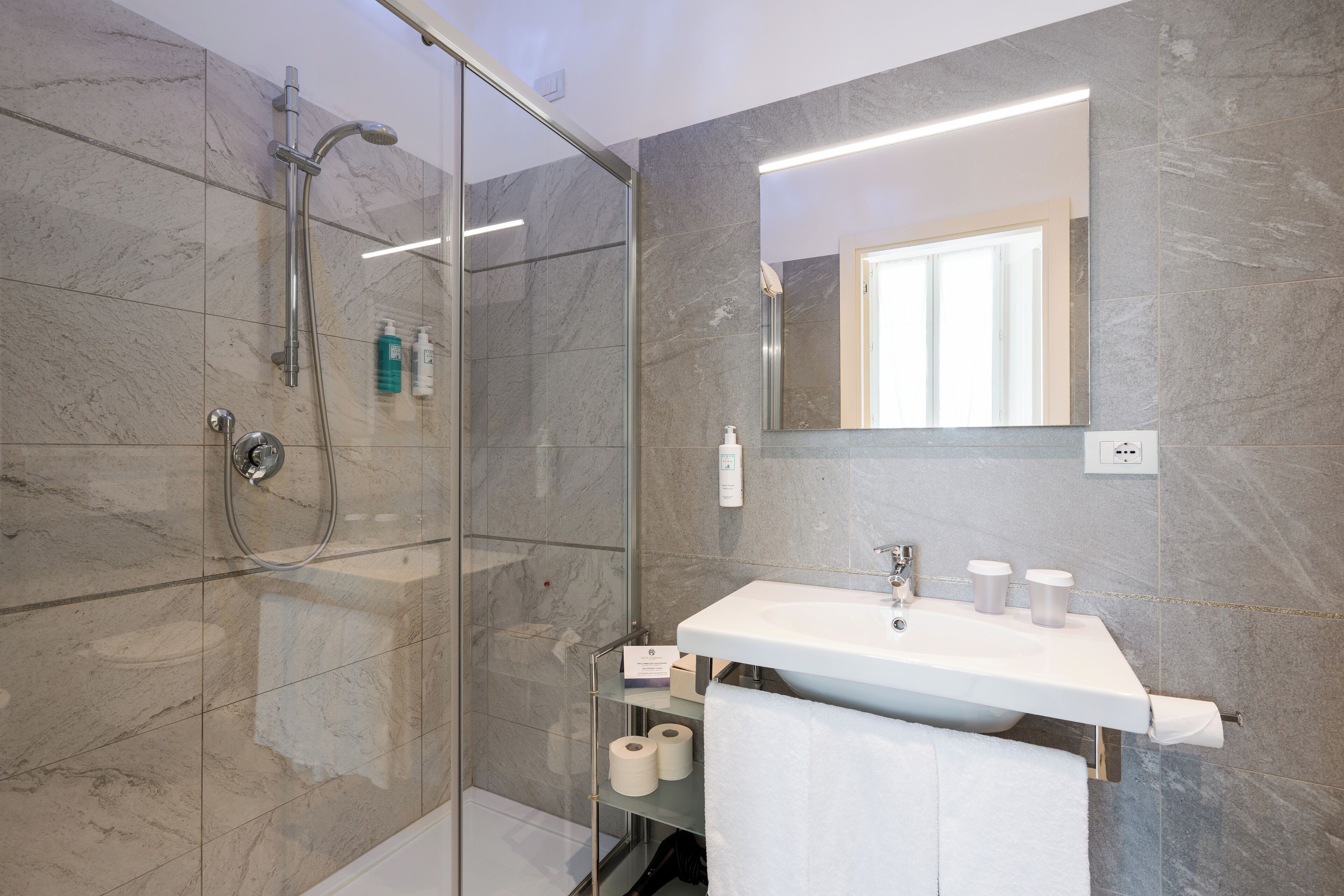 A modern bathroom with a glass-enclosed shower, a white sink, and marble walls.