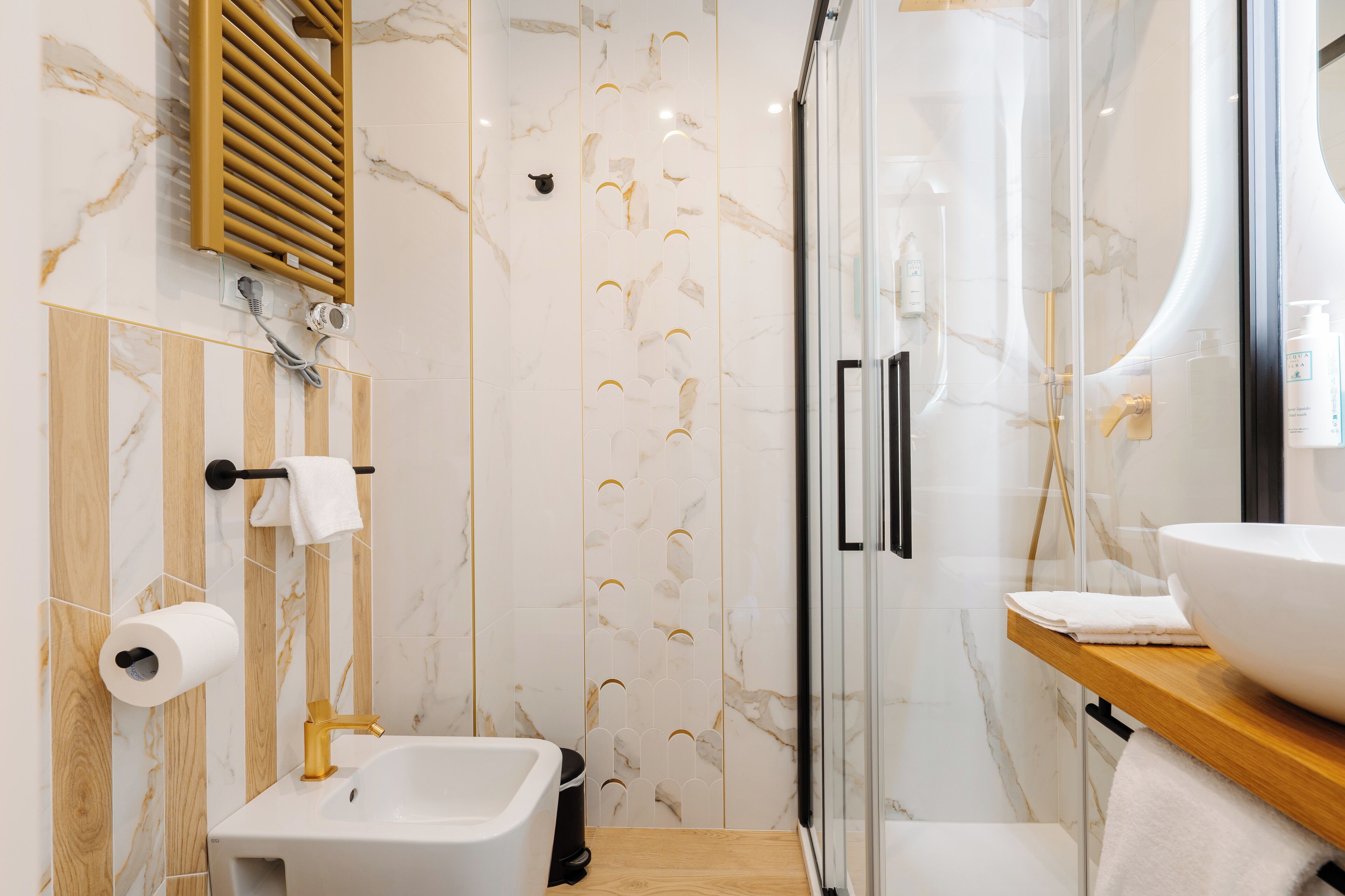 A modern bathroom with a marble backsplash, a glass shower enclosure, a wooden vanity, and a white sink.