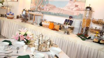 A breakfast buffet setup with various food items and beverages, a decorative painting on the wall, and a neatly arranged table with dining ware.