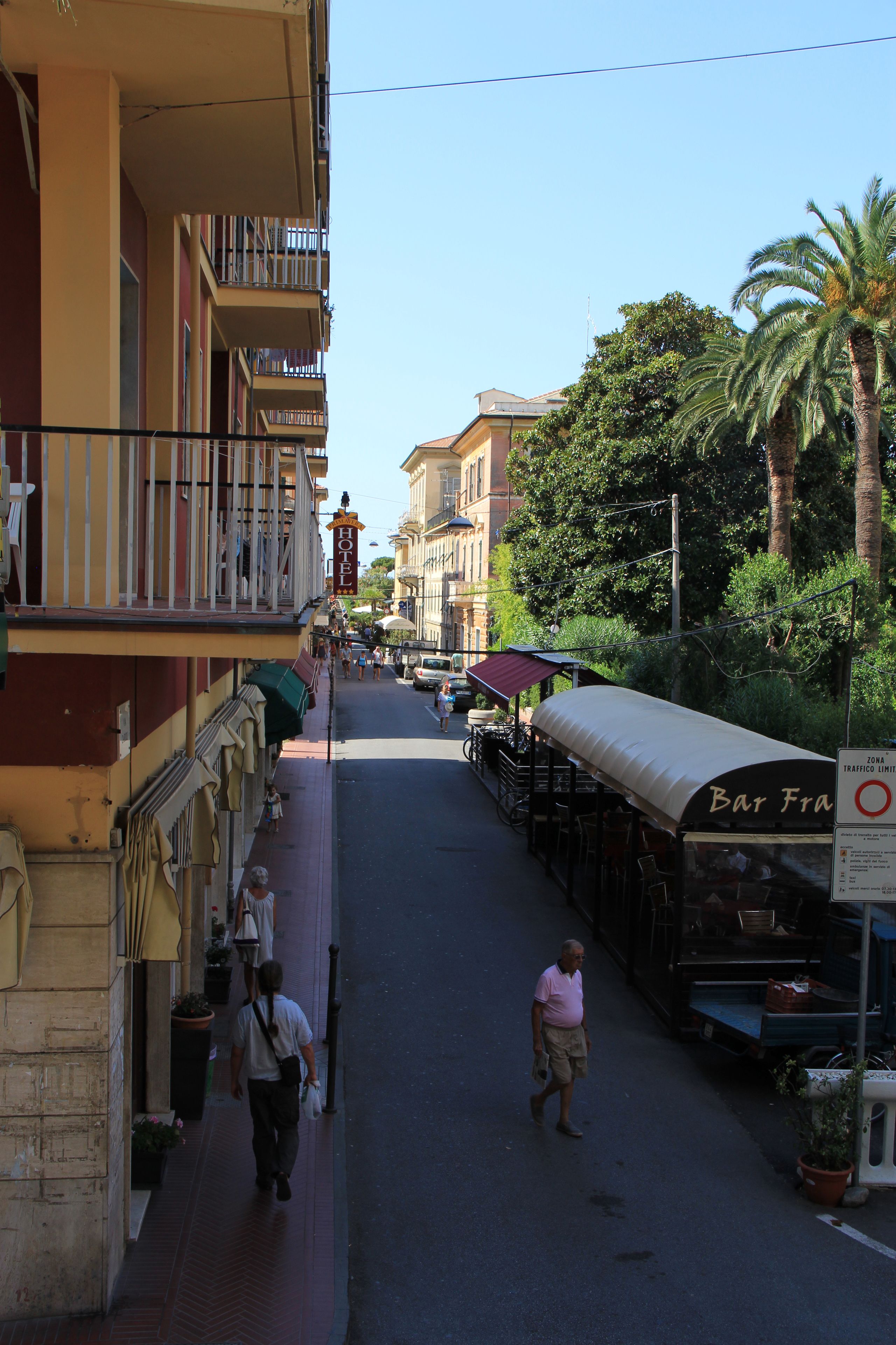 Una calle con un bar llamado "Bar Fra" y un edificio con balcones.