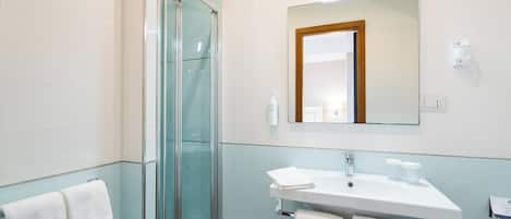 A modern bathroom with a glass shower enclosure, a white sink with two towels, and a mirror with a wooden frame.