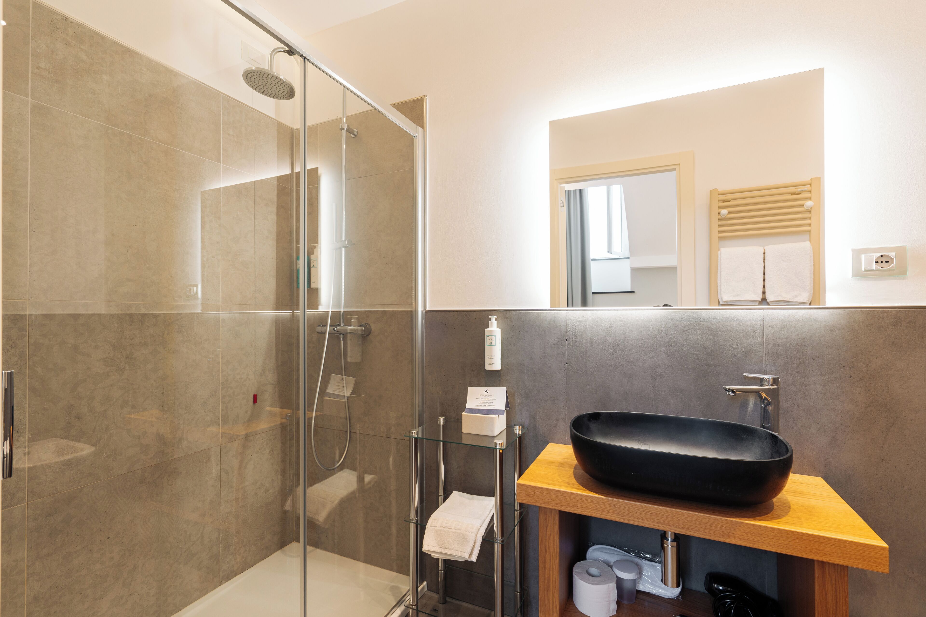 A modern bathroom with a glass-enclosed shower, a black vessel sink, and a wooden vanity.