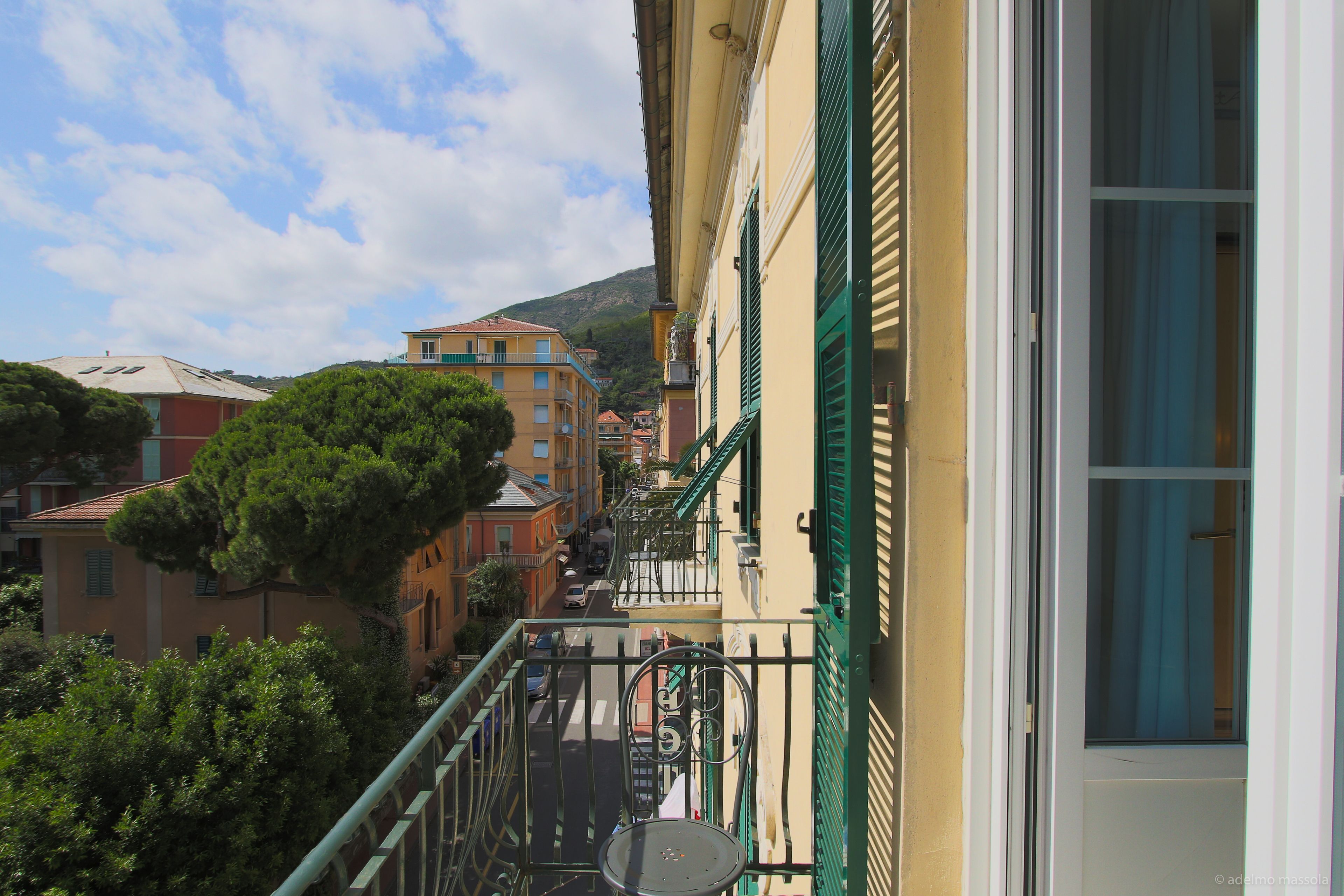A balcony with a metal chair, a satellite dish, and a view of a street with buildings and trees.
