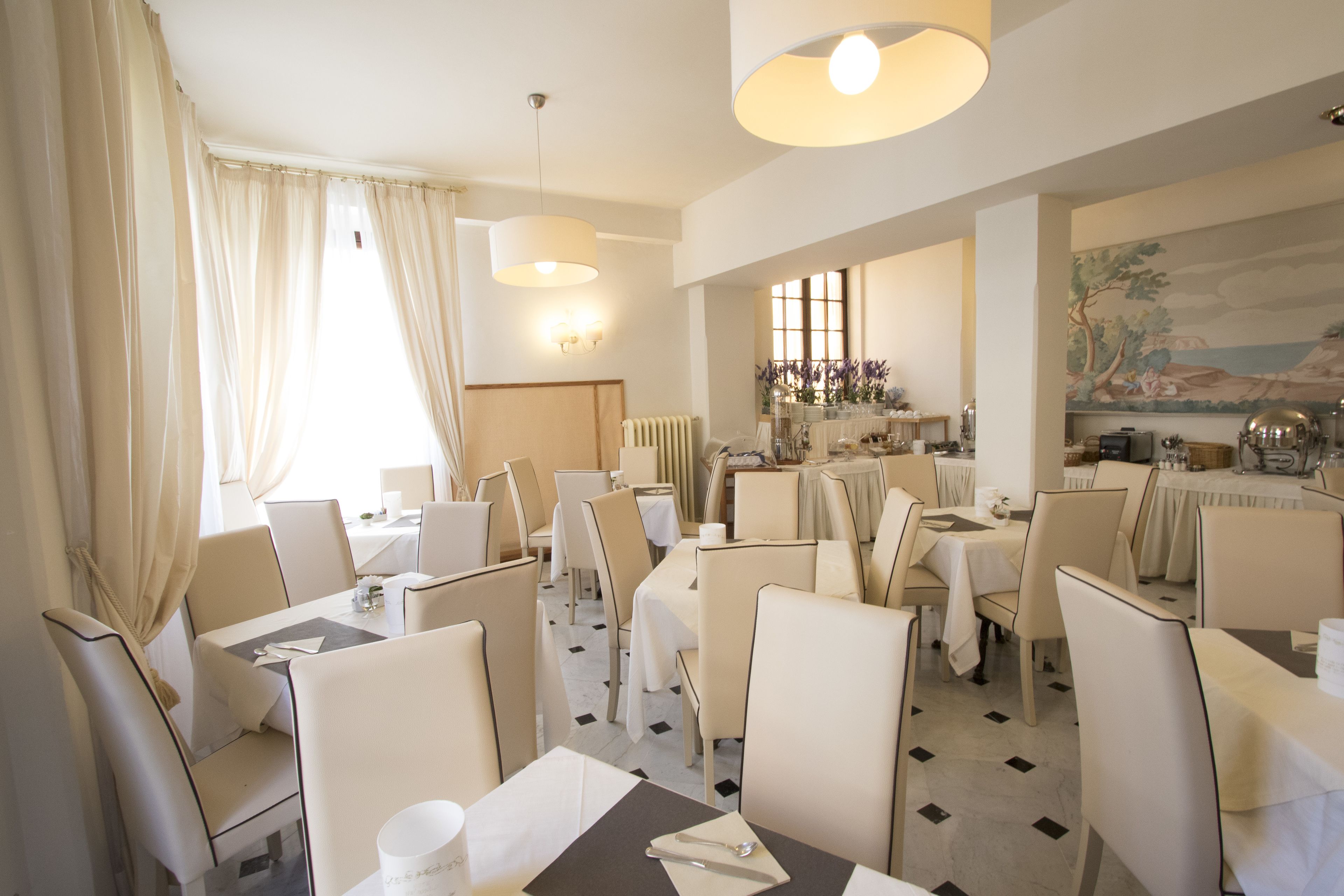 A dining area with multiple tables and chairs, a chandelier, and a mural on the wall.