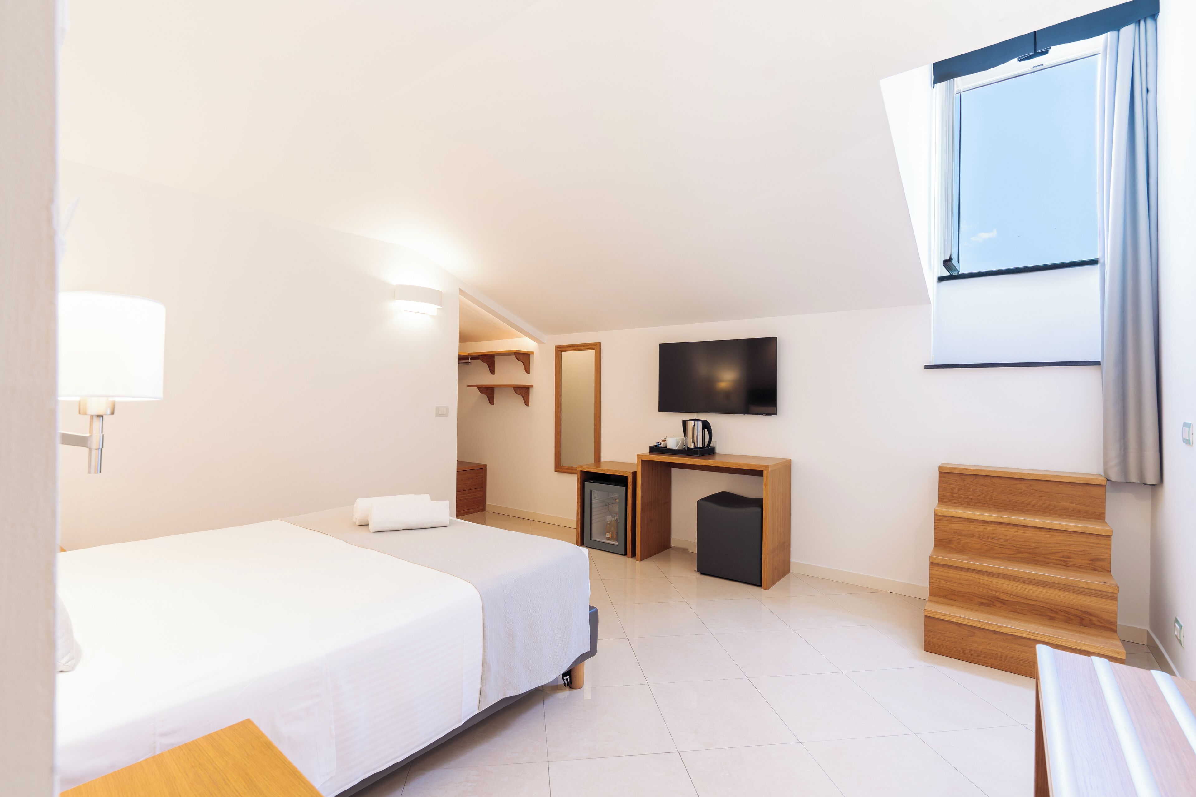 Una habitación de hotel con cama, escritorio, televisión y ventana con cortinas.
