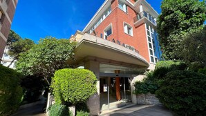 L’entrée d’un hôtel, avec une allée couverte, un ciel dégagé et une végétation luxuriante tout autour.