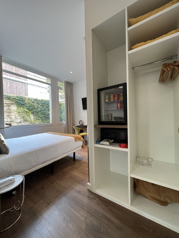Une chambre d’hôtel moderne équipée d’un lit, d’une télévision, d’une armoire et offrant une vue sur la verdure environnante.