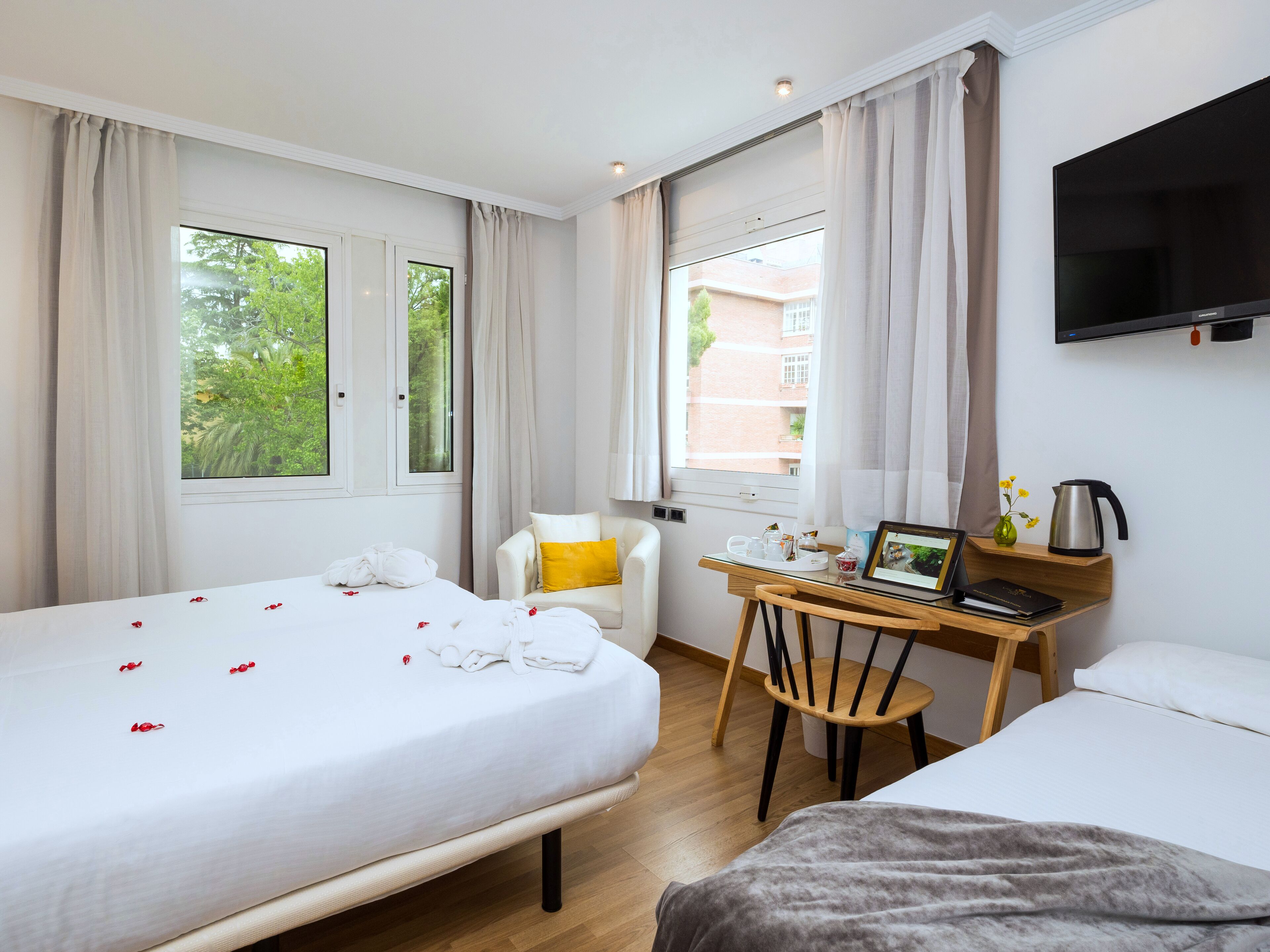 A hotel room with two beds, a desk with a laptop, a chair, and a TV on the wall.
