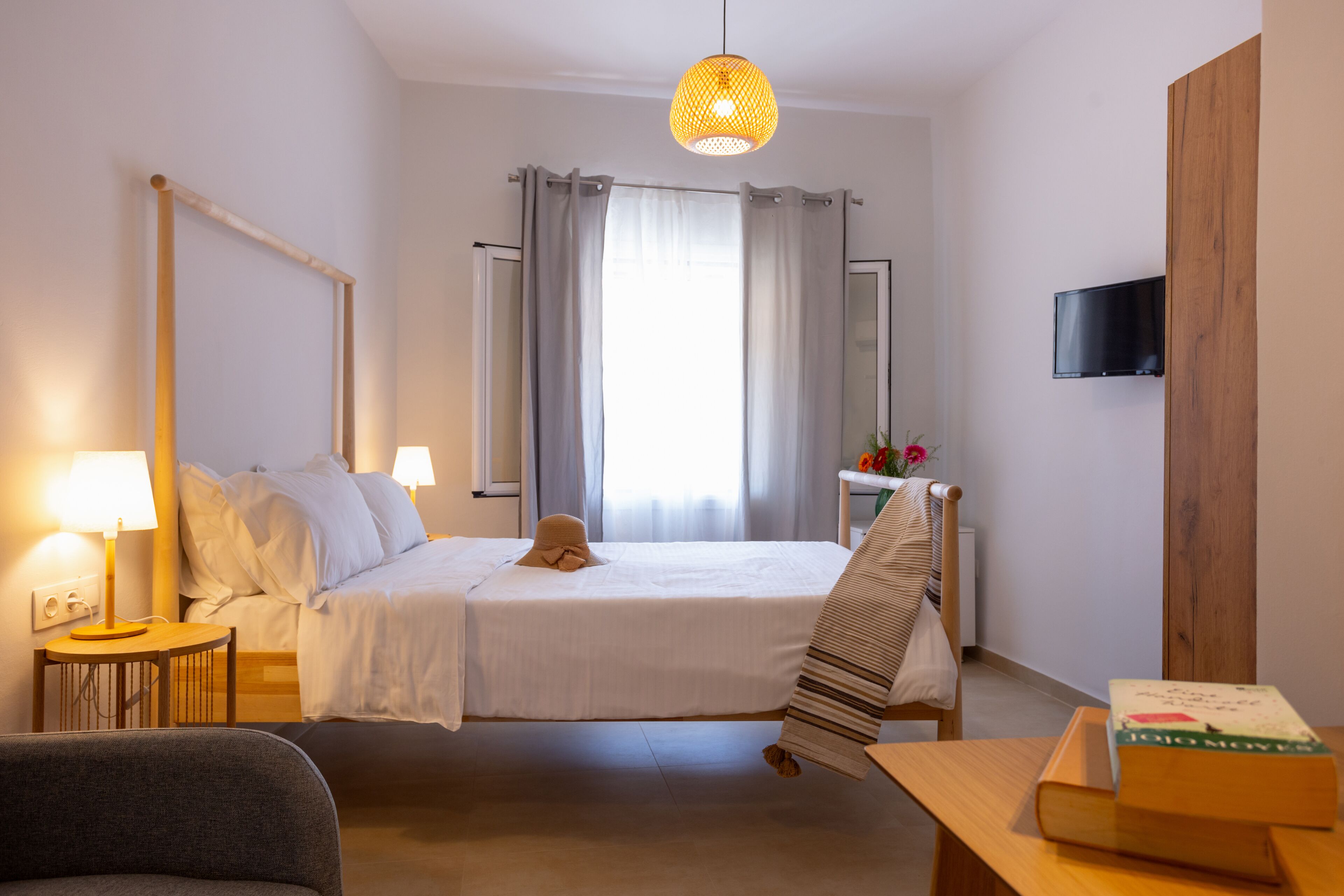 A hotel room with a bed, bedside tables, a TV, and a window with curtains.