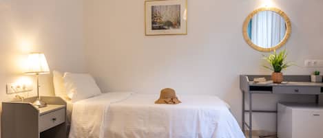 A neatly arranged bedroom with a bed, bedside table, lamp, and a desk with a mirror and plants.