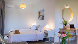 Habitación de hotel con dos camas, un escritorio con una computadora portátil, un espejo y un florero con flores.