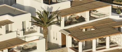 A modern multi-story residential building with a balcony, a palm tree, and a stone wall.