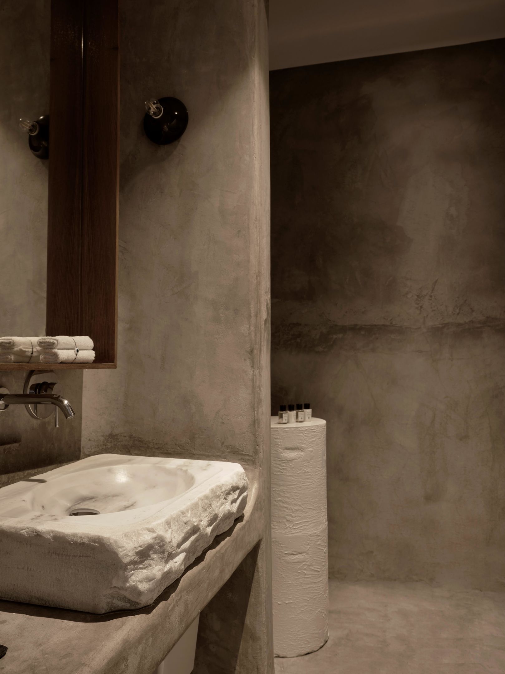 Un baño con lavamanos de mármol, un armario de medicinas de madera y un rollo grande de papel higiénico.