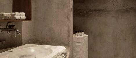 Un baño con lavamanos de mármol, un armario de medicinas de madera y un rollo grande de papel higiénico.