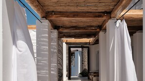 Un pasillo con vigas de madera y cortinas blancas que conduce a una habitación con pared de piedra y vista al cielo.