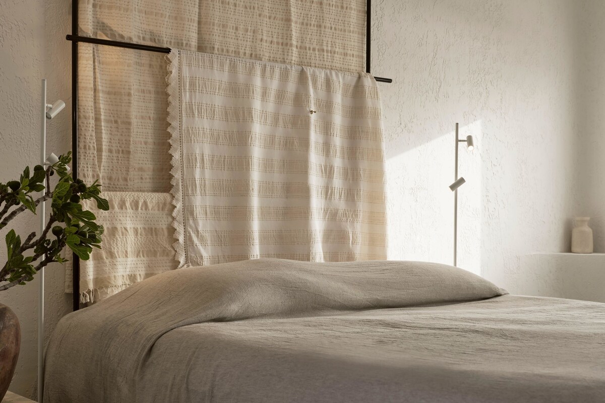 Ein Schlafzimmer mit einem Bett, Vorhängen, einem Nachttisch, einer Lampe und einer Pflanze.