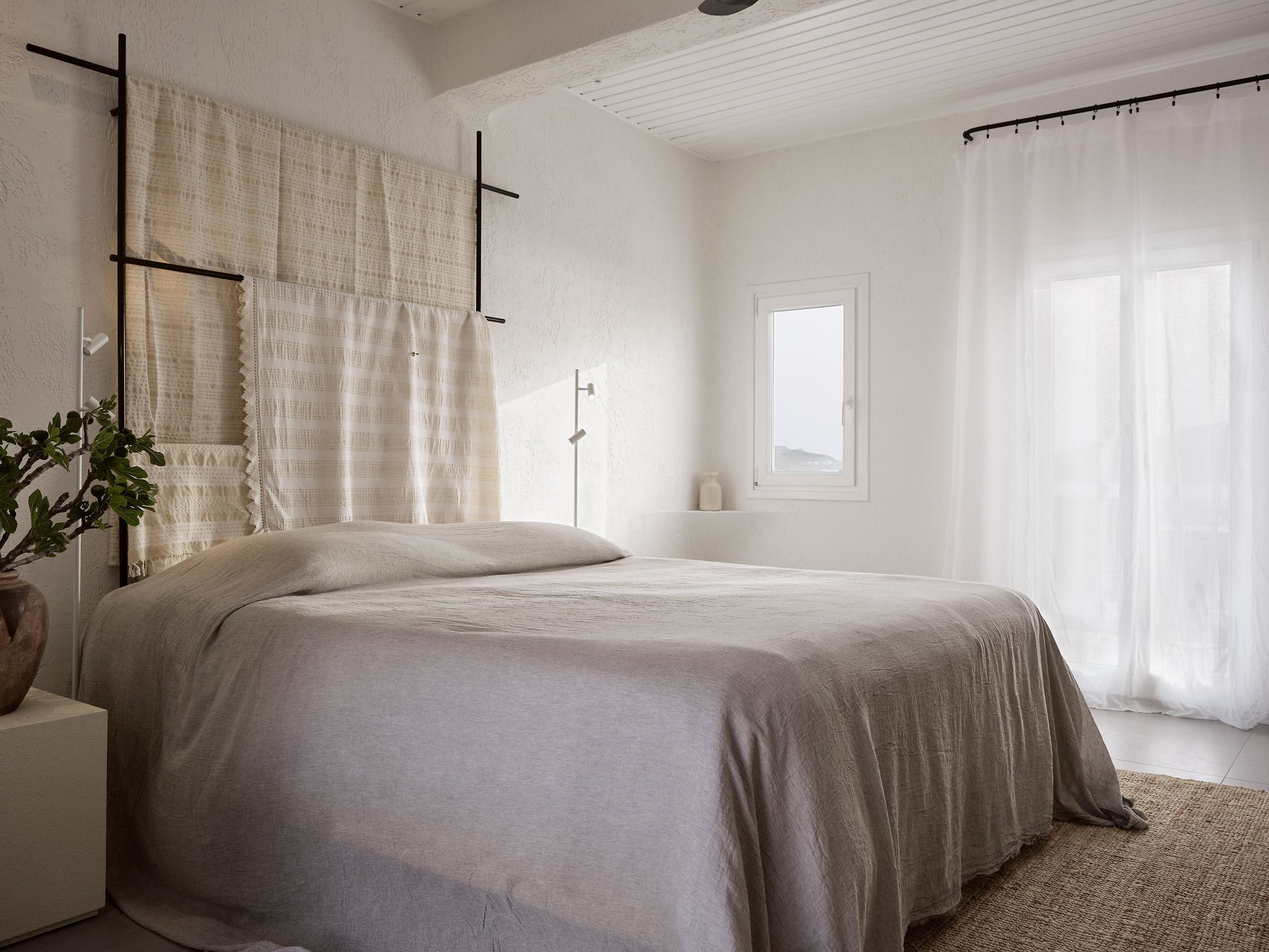 Un dormitorio minimalista con cama, mesita de noche, lámpara de pie y ventana con cortinas.