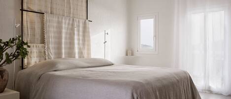 Un dormitorio minimalista con cama, mesita de noche, lámpara de pie y ventana con cortinas.